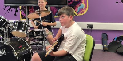 Two boys in a band, one on drums, one with a guitar